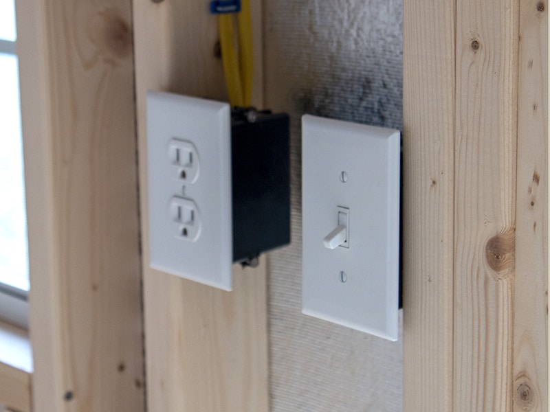 Two electrical outlets and an electrical switch on the wall of shed.