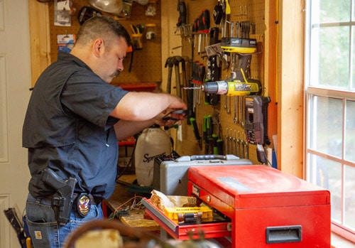 A man works on a workbench in his outdoor building shed.
